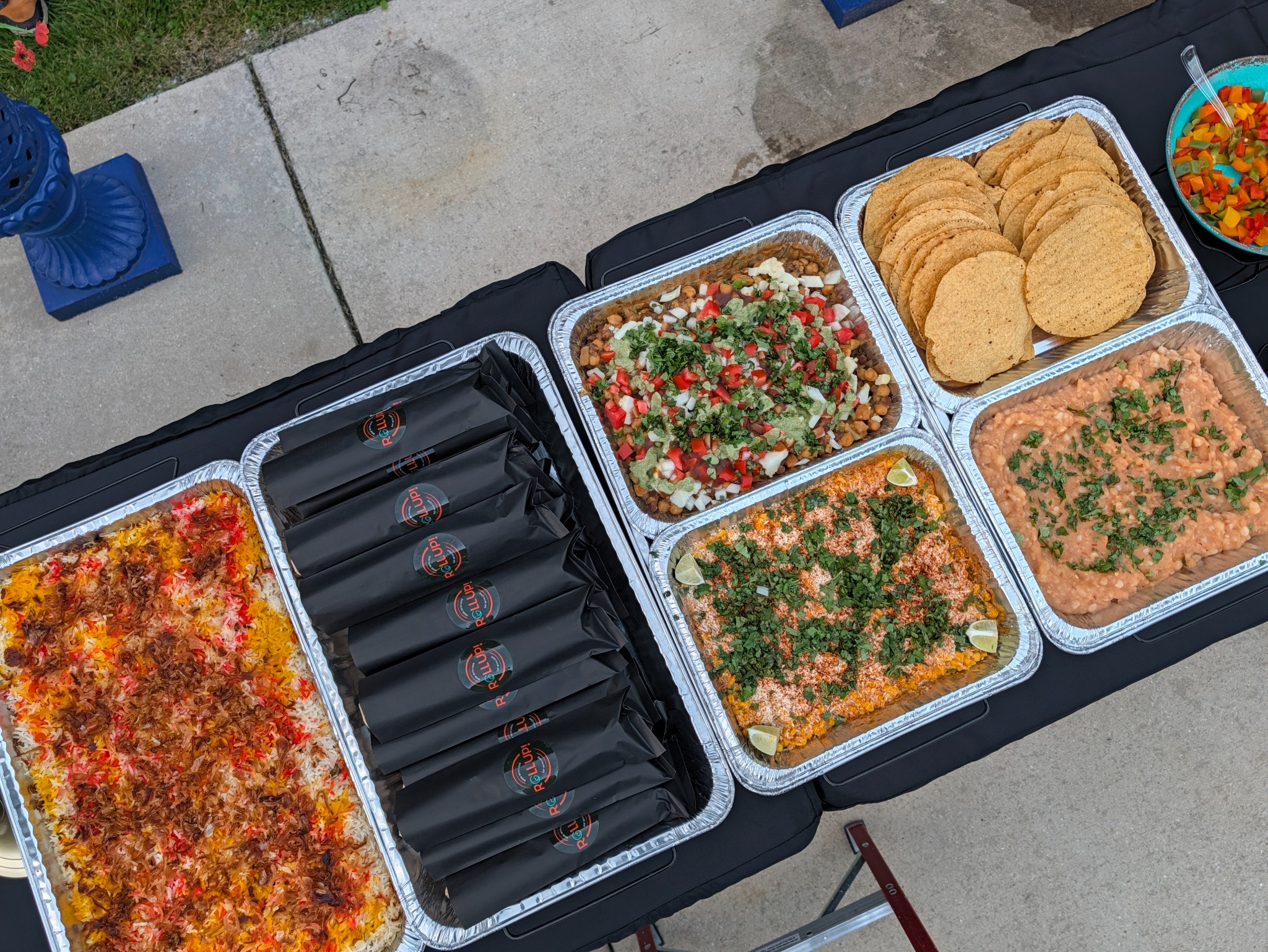 Rollup catering spread with wrapped rolls, rice, chaat, corn, and tostadas
