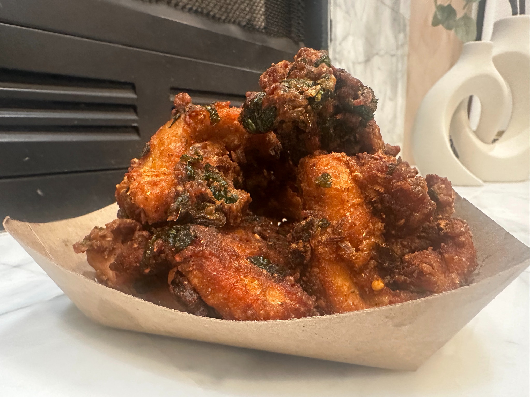 Crisp, spiced Chicken 65 bites served in a paper tray